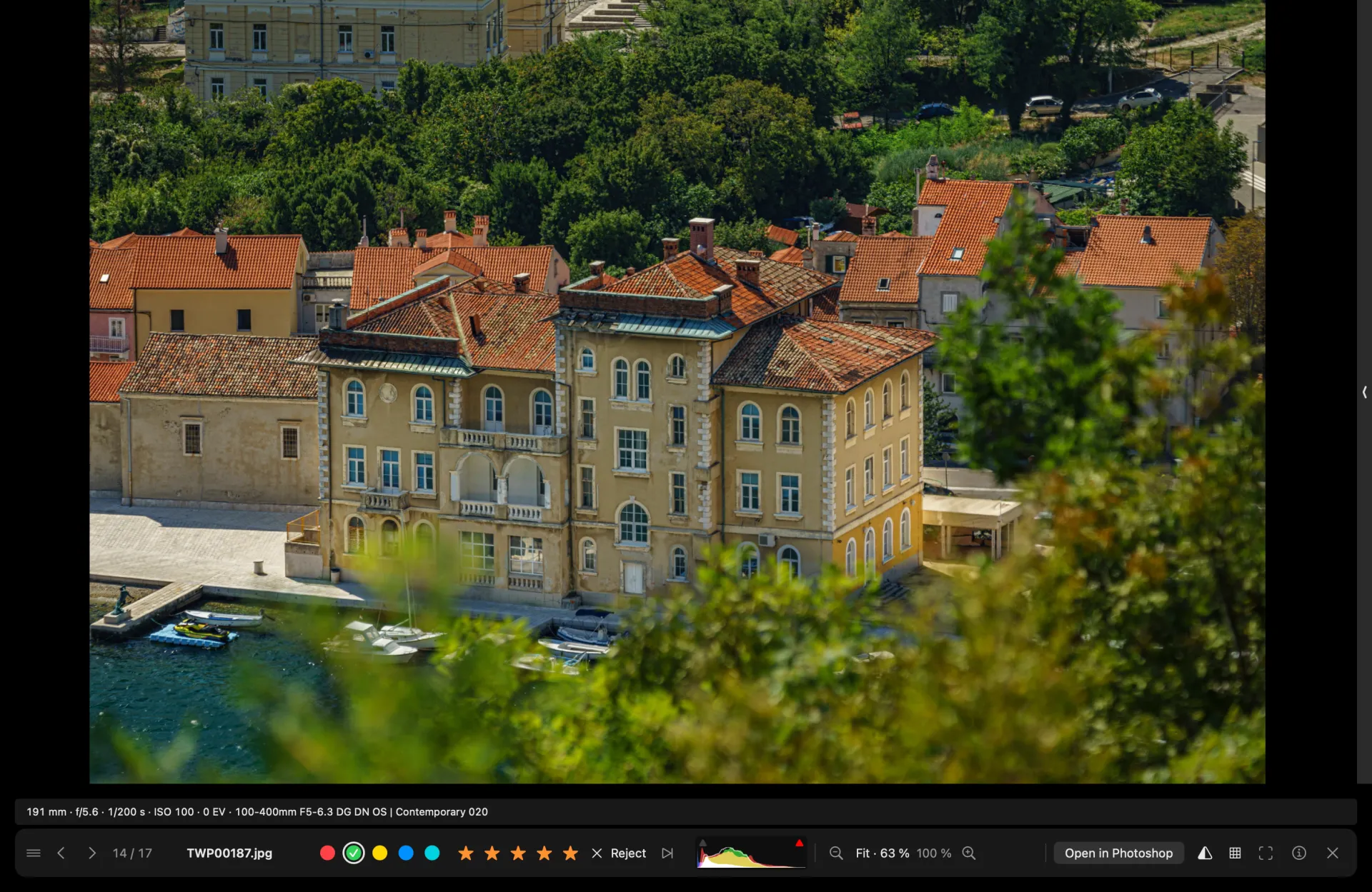 The full-screen viewer: a harbour town photo edge to edge, an info line with focal length, aperture, shutter speed and lens, and a control bar with labels, stars, a small histogram and the zoom